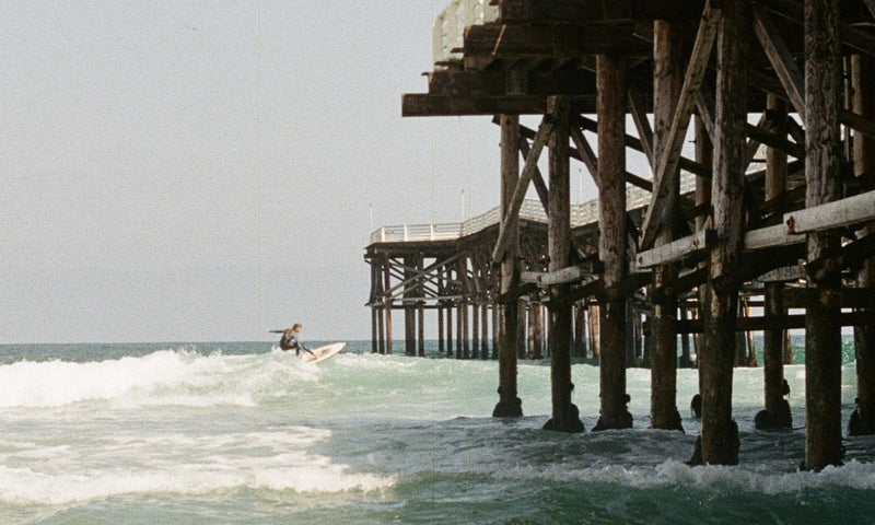 Surfer riding a wave near a pier on a sunny day