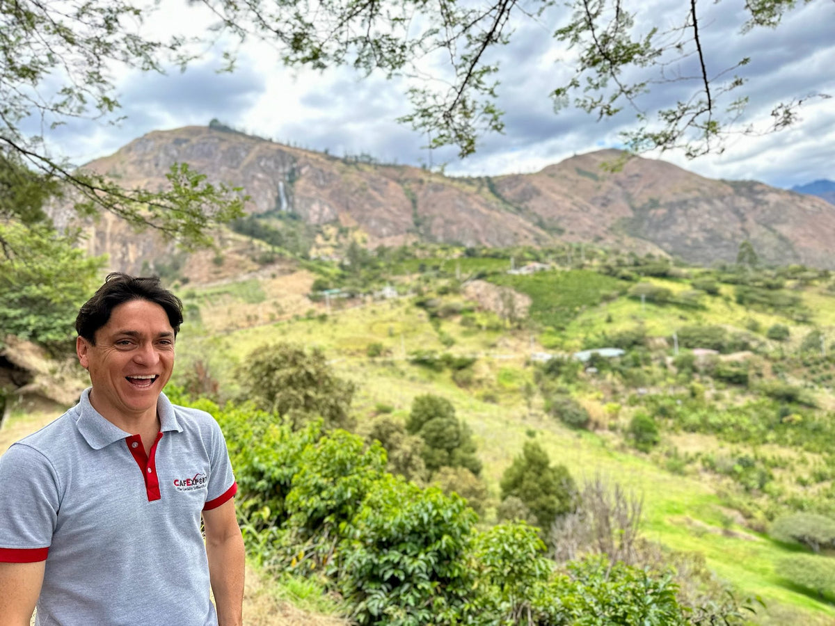 A laughing coffee producer in front of coffee trees and a dry Andean ridge